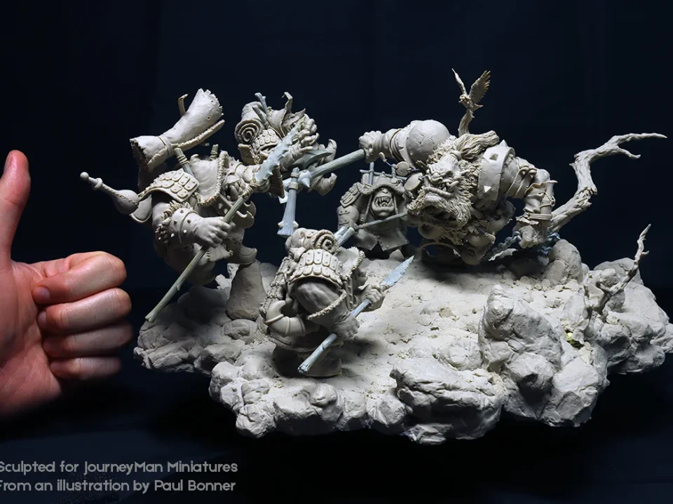Hand holding a detailed miniature sculpture of people on a rock, titled 'Journeyman Miniatures' by Paul Bonner