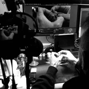 Black-and-white portrait of a man with glasses sitting at a desk, holding a sculpted object