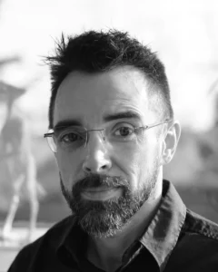 Man with glasses, beard, and shirt standing in front of a blurred background