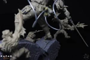 Close-up of a detailed hand-sculpted statue of a man holding a sword, labeled 'KAZAM' and 'Atelier'